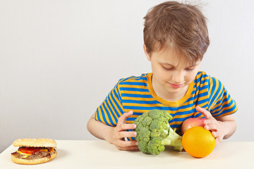 Young boy at the table chooses between hamburger and healthy diet on a white background