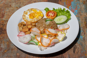 Fried rice with vegetables, rice chips, cheese tofu and fried egg on the old wooden table in local cafe, close up indonesian cuisine. Breakfast in Bali, Indonesia