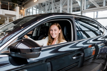 Fototapeta na wymiar Happy girl sitting in a new bought black car in a car dealership