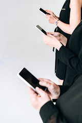 cropped view of businesswomen in total black outfits using smartphones isolated on grey