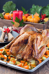 Thanksgiving roasted turkey with vegetables, carrot, parsnip, potato on a tray. Autumn decorations with leaves, rowan berries and pumpkins in a wooden box on background, vertical