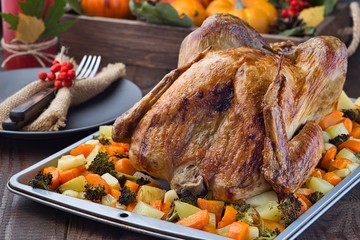 Thanksgiving roasted turkey with vegetables, carrot, parsnip, potato on a tray. Autumn decorations with leaves, rowan berries and pumpkins in a wooden box on background, horizontal