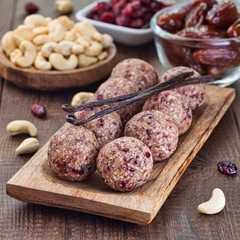Healthy homemade energy balls with cranberries, cashew nuts, dates and vanilla on a wooden plate, square format