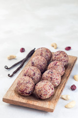 Healthy homemade energy balls with cranberries, cashew nuts, dates and vanilla on a wooden plate, vertical,  copy space