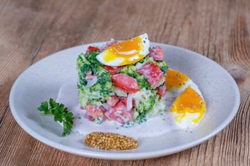 Delicious salad with broccoli, tomato, onion and boiled egg with cream sauce in plate on wooden background. Healthy food