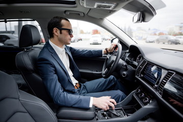 Adult male sitting behind the wheel of a car switching speed on the gearbox