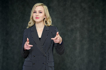 Portrait of a pretty young blonde girl with beautiful hair, excellent make-up, perfect face skin in a business suit on a dark background. Made in the studio.