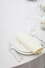 empty table served by white tablecloths, white plates, cutlery and glasses ready to receive guests in selective focus