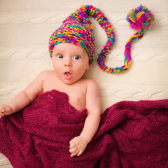 Close portrait of adorable baby in knitted funny gnome hat lies on his back.