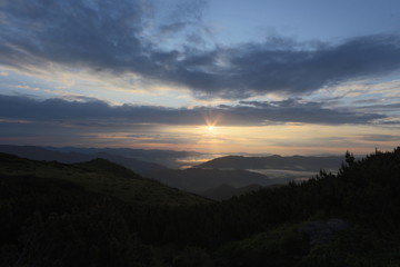 the top a mountain landscape under the rays of the rising sun, the light that illuminates the peaks of the mountain range of the valley covered with a gentle milky fog