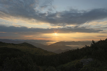 Fototapeta premium the top a mountain landscape under the rays of the rising sun, the light that illuminates the peaks of the mountain range of the valley covered with a gentle milky fog