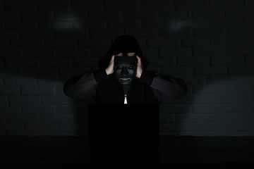 Hacker in black mask and hood at the table