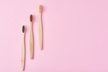 three wooden bamboo toothbrushes on a pink background, top view.  Dental care concept