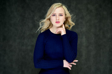 Portrait of a pretty young slim blonde girl with beautiful fluttering hair, great makeup, in a dark blue dress on a dark background. Made in the studio.