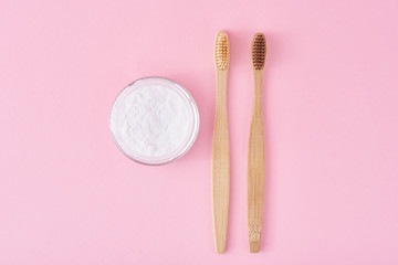 Two wooden bamboo toothbrushes and baking soda powder in glass jar on a pink background.  Teeth health and keep mouth concept