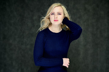 Portrait of a pretty young slim blonde girl with beautiful fluttering hair, great makeup, in a dark blue dress on a dark background. Made in the studio.