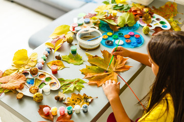 Little girl painting on autumn yellow leaves with gouache, kids arts, children creativity, autumn art.