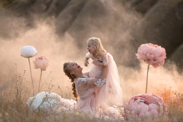 Mom and daughter in pink fairy-tale dresses play in a field surrounded by Big pink decorative flowers