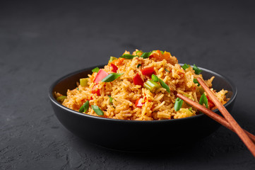 Veg Schezwan Fried Rice in black bowl at dark slate background. Vegetarian Szechuan Rice is indo-chinese cuisine dish with bell peppers, green beans, carrot.