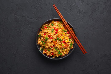 Veg Schezwan Fried Rice in black bowl at dark slate background. Vegetarian Szechuan Rice is indo-chinese cuisine dish with bell peppers, green beans, carrot. Copy space. Top view