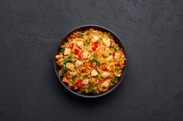 Schezwan Chicken Fried Rice in black bowl at dark slate background. Szechuan Rice is indo-chinese cuisine dish with bell peppers, green beans, carrot, chicken breasts. Copy space. Top view