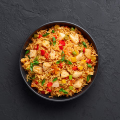 Schezwan Chicken Fried Rice in black bowl at dark slate background. Szechuan Rice is indo-chinese cuisine dish with bell peppers, green beans, carrot, chicken breasts. Copy space. Top view
