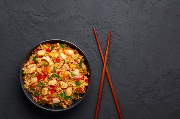 Schezwan Chicken Fried Rice in black bowl at dark slate background. Szechuan Rice is indo-chinese cuisine dish with bell peppers, green beans, carrot, chicken breasts. Copy space. Top view
