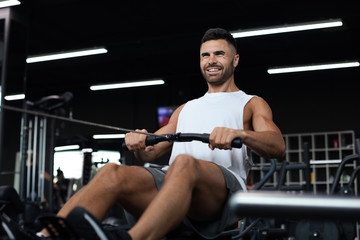 Fit and muscular man using rowing machine at gym.