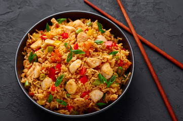 Schezwan Chicken Fried Rice in black bowl at dark slate background. Szechuan Rice is indo-chinese cuisine dish with bell peppers, green beans, carrot, chicken breasts.