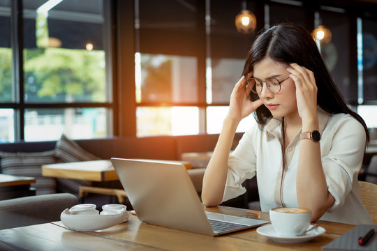 Freelance asian woman headache tired,stess or deadline with digital laptop computer working on workplace in coffee shop.