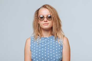 Naklejka premium Portrait of a girl in round glasses and a blue dress on a light gray background