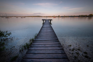 Fototapeta na wymiar Small wooden bridge with a person meditating in the background on an Ammersee lake in Bavaria