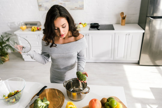 Overhead View Of Beautiful Girl Holding Glass Lid And Looking At Saucepan