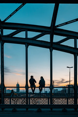 Backlight of several people sitting waiting for the sunset on the Hacker bridge located in Munich