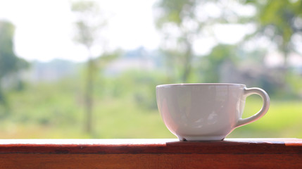 Close up white coffee cup on wood table and view of morning