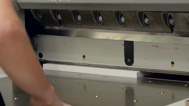 Worker in the printing house cuts a pack of paper on a machine making business cards