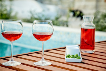 two glasses of rose wine with  olives against blue water on a pier..