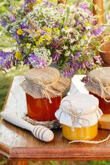 Fototapeta na wymiar Jars with honey and bouquet of wild flowers in the garden.