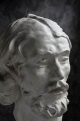 Fototapeta na wymiar Gypsum copy of ancient statue John the Baptist head on dark textured background. Plaster sculpture man face.