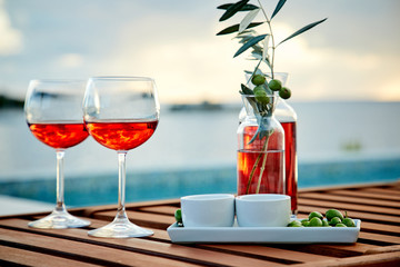 two glasses of rose wine with  olives against blue water on a pier..