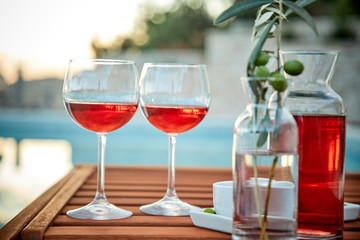 two glasses of rose wine with  olives against blue water on a pier..