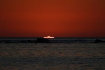 sun reaching the horizon in the sea on a red sky sunset