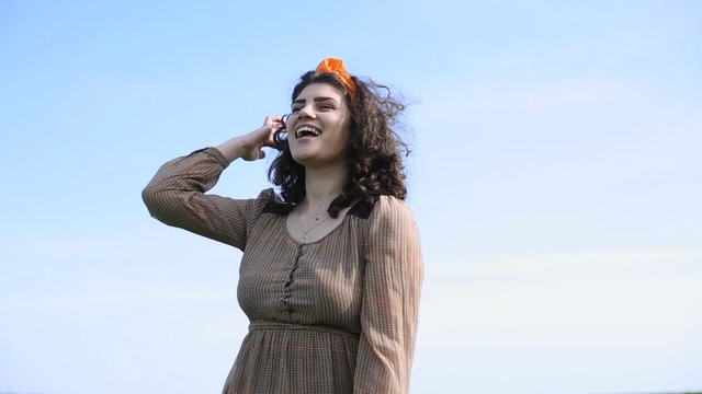 Close plan of pretty smiling  young woman with curly hair dressed in brown dress turning around  and looking far on the background of sky. Beautiful plus-size model posing.