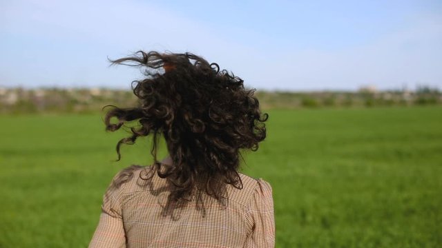 Close plan of pretty smiling  young woman with curly hair dressed in brown dress dancing and running in the green feeld. Beautiful plus-size model posing.