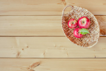 Red apples in a wicker basket on a wooden background. Autumn harvest. Flat lay. Selective focus. Copy space.	
