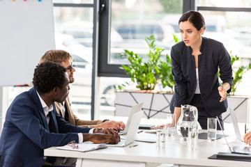multiethnic businesspeople at table with laptops during conference in office