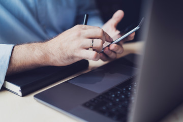 Person installing app on smartphone. Man dialing phone number on mobile device. Male specialist using smartphone and laptop at workplace for developing digital projects, getting corporate online data.