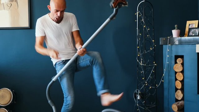 Funny man playing vacuum cleaner like guitar while cleaning house. Crazy emotions. 4K slow motion video.