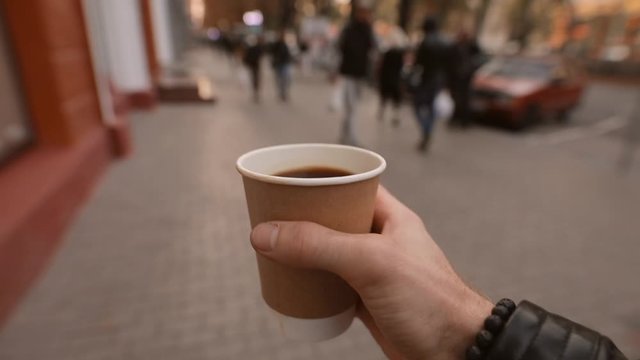 1st Person View, Man Holding And Carries Paper Coffee Cup Walking Along City Street