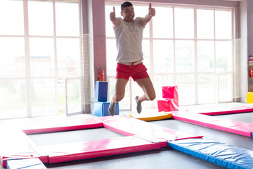Fototapeta premium Fitness, fun, leisure and sport activity concept - Handsome happy man jumping on a trampoline indoors